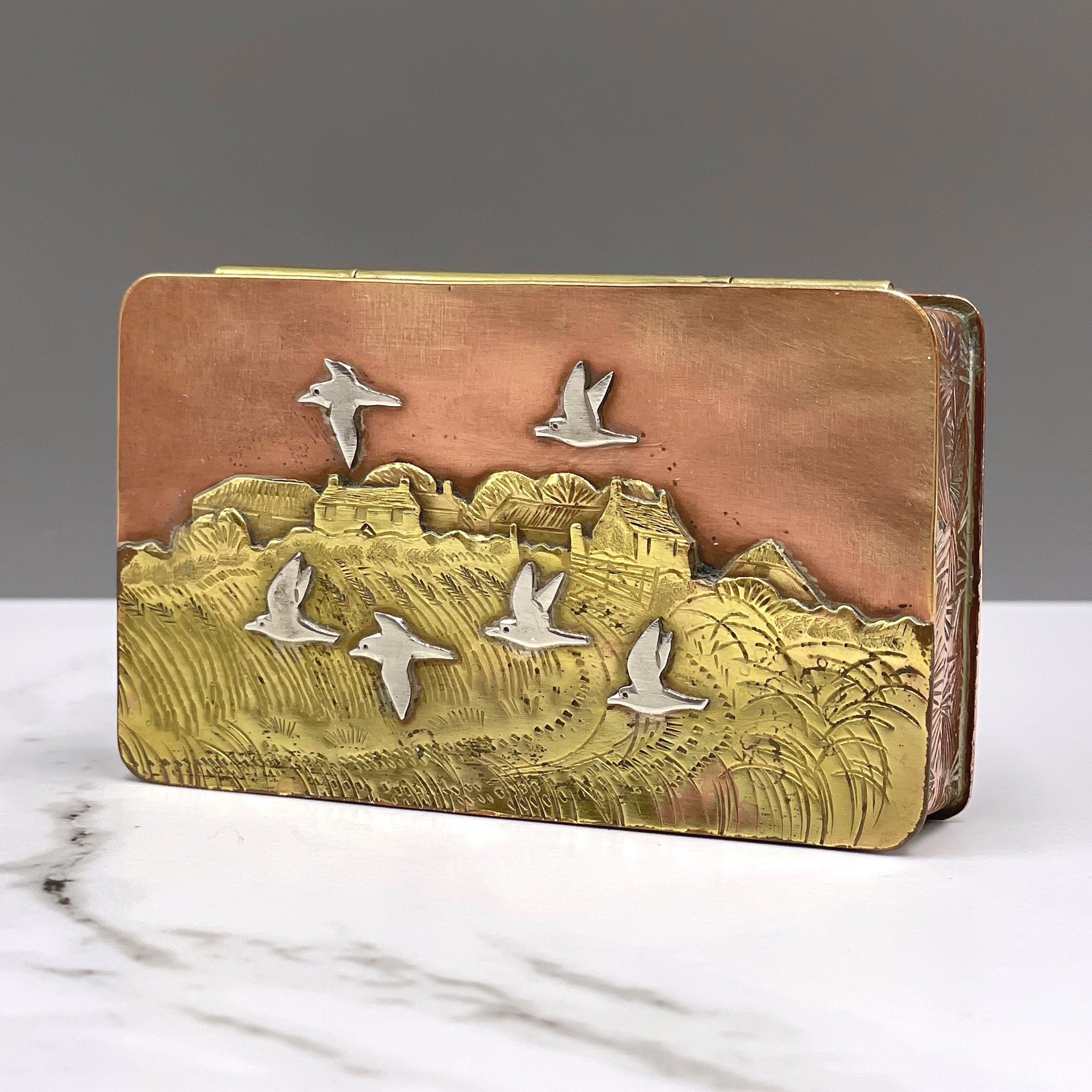 Metal hinged box depicting birds flying over a wheat field near a farmhouse by artist Cornelius Van Dop