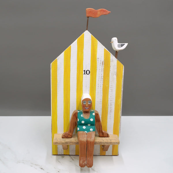 Driftwood sculpture of a lady sitting outside a beach hut as a seagull watches on by artist Lynn Muir