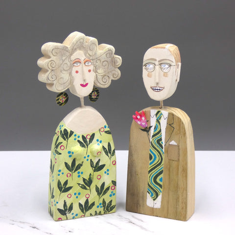 Driftwood sculptures of a man wearing a suit with a colourful tie and a woman wearing a dress and earrings with matching colours by artist Lynn Muir