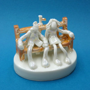 Porcelain sculpture of a couple and a bird sitting on a bench by artist Andrew Bull