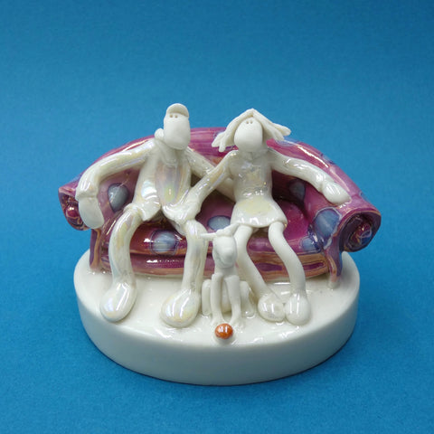 Porcelain sculpture of couple sitting on the sofa with a dog by artist Andrew Bull
