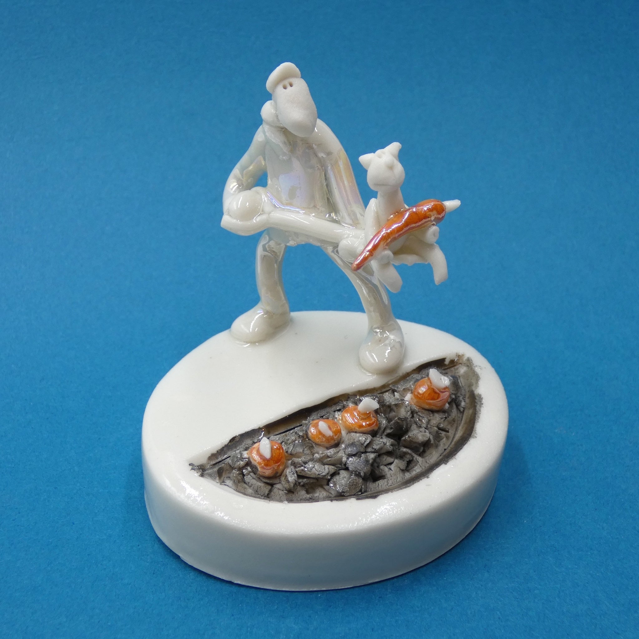 Porcelain sculpture of a man tending the carrots with help from his cat by artist Andrew Bull